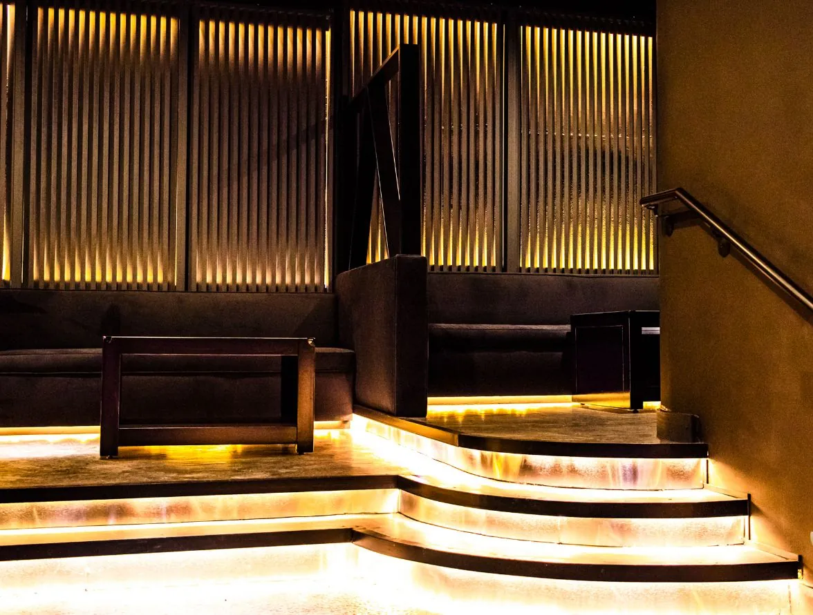 Gold under-lit terraced VIP steps and slat walls inside West Eight